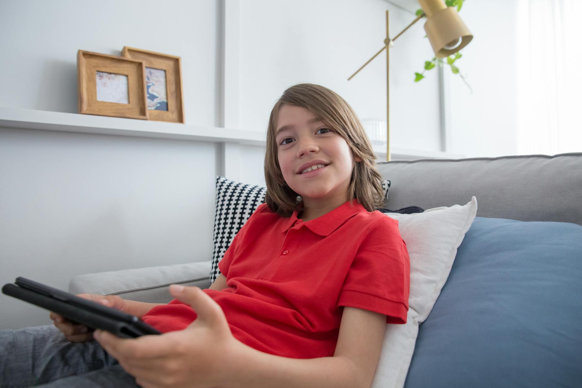 Chłopiec w czerwonej koszulce korzysta z tabletu w domu