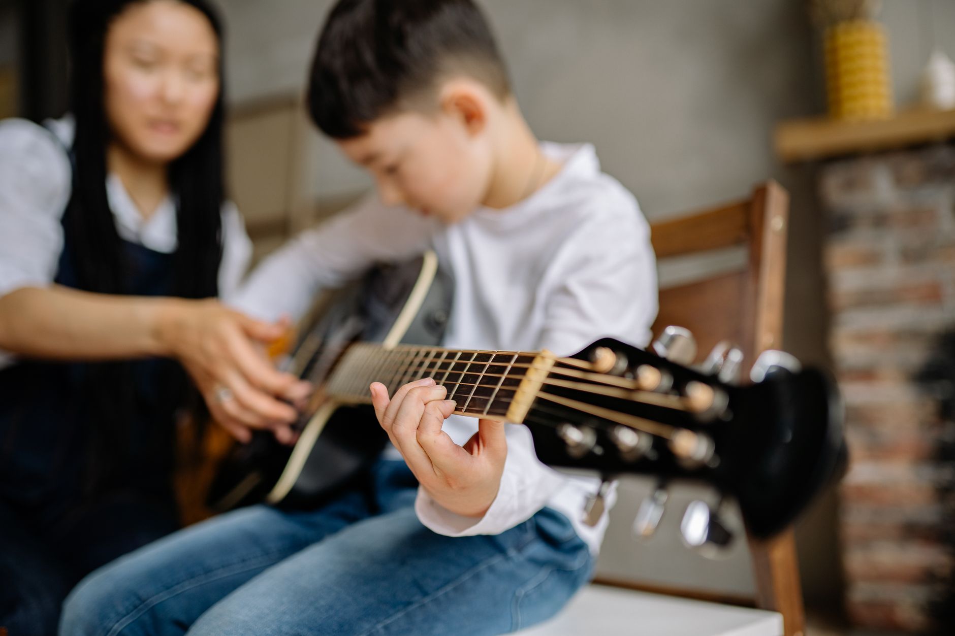 Chłopiec uczy się gry na gitarze akustycznej z pomocą opiekuna