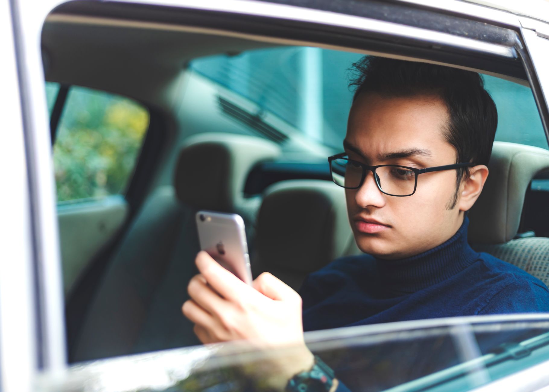 Mężczyzna w okularach korzysta ze smartfona w zaparkowanym Fordzie Focus
